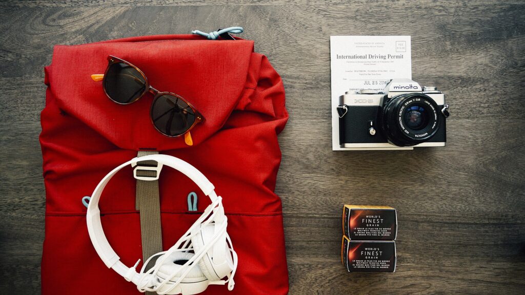 Mochila de viaje roja con ropa, cámara y gafas de sol
